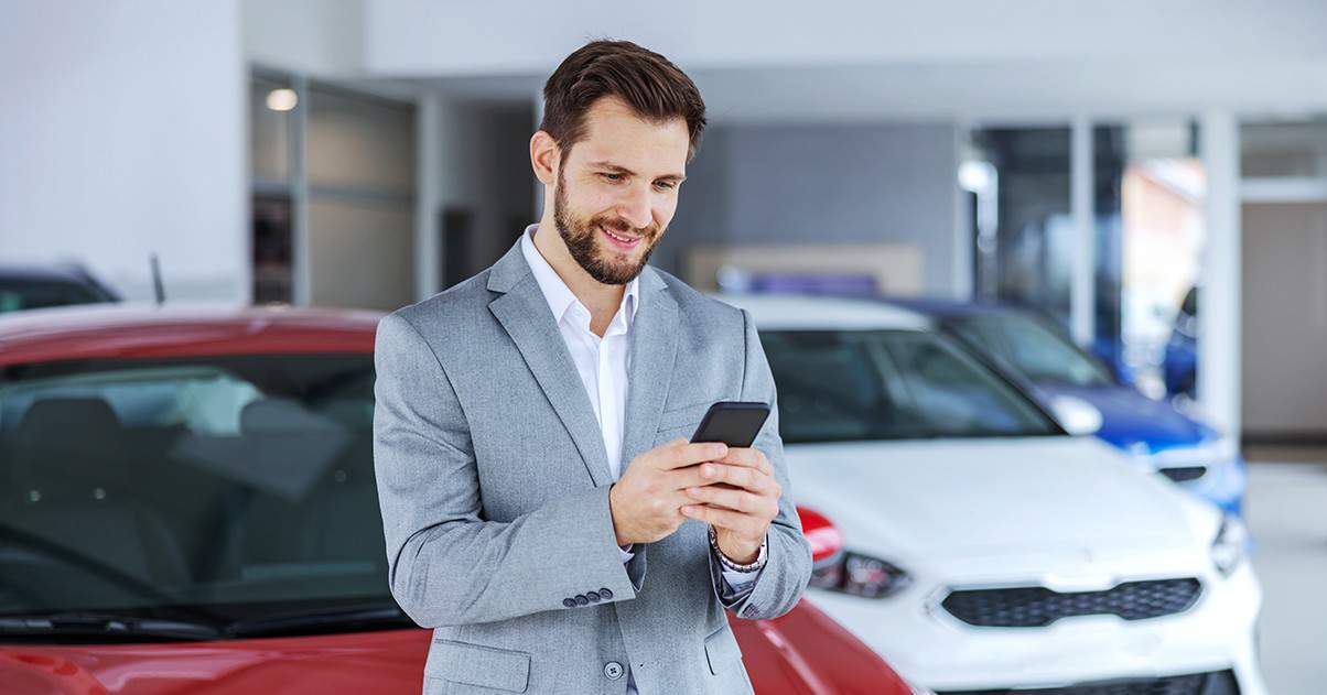 Business man in an automotive dealership using his cell phone.