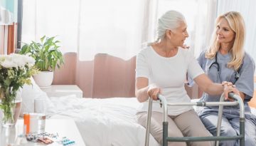 Healthcare professional helping a senior woman use her walker to get out of bed.